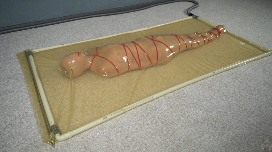 Mummification with bandages and rope bondage with ankle brace in a vacuum bed