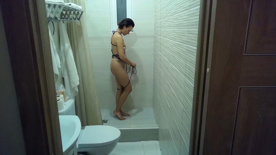Sofi in a black rope harness washes in the shower POV